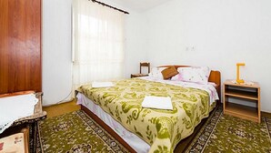 Quarto com cama, mesa de cabeceira de madeira, cadeira e janela com cortinas.