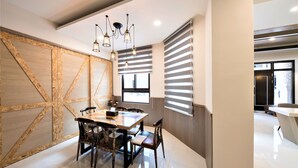 A modern dining area with a wooden accent wall, a chandelier, and a view of the adjacent kitchen. - Clear Sky Laurel B&B (Magong)