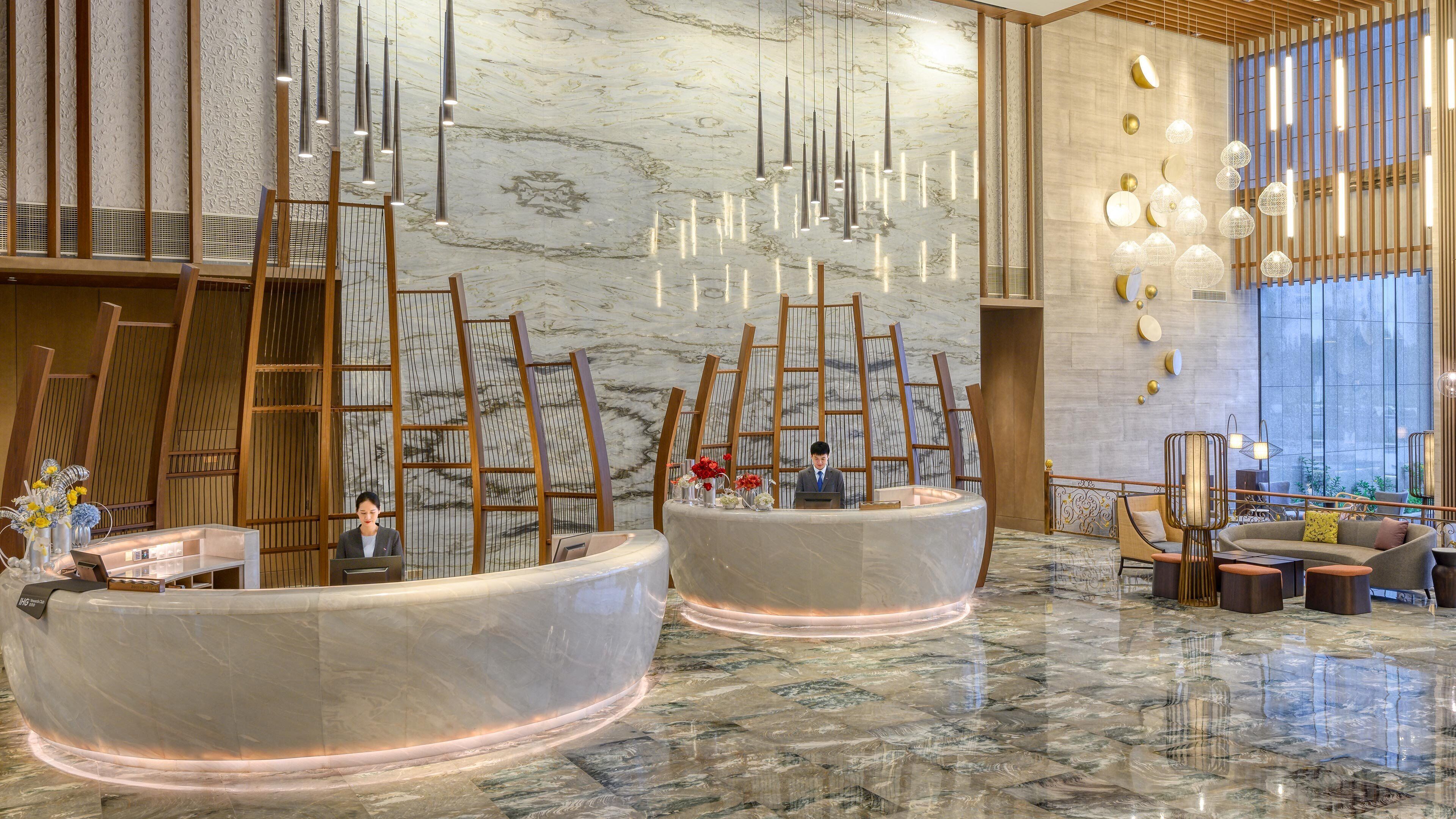 Un moderno vestíbulo de hotel con piso de mármol, una recepción y luminarias contemporáneas.