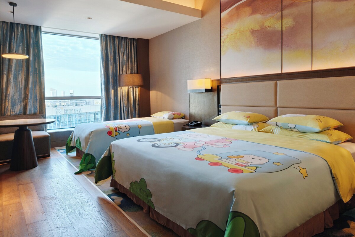 Una habitación de hotel con dos camas, un escritorio y vista a la ciudad.