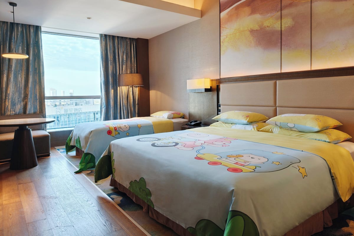 A hotel room with two beds, a desk, and a view of the city.