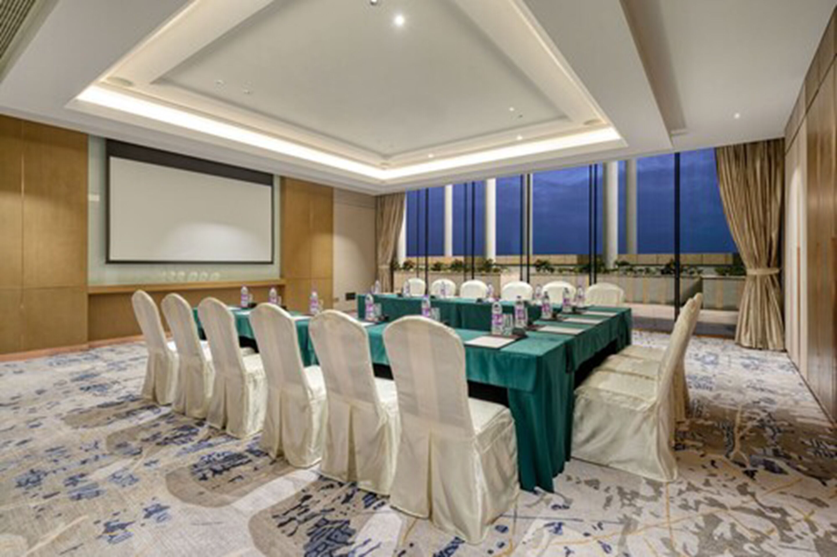 A conference room with a long table, white chairs, and a projector screen.