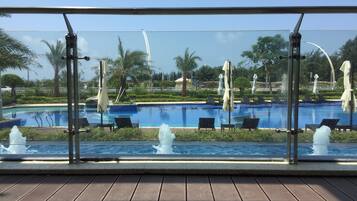A pool area with lounge chairs and umbrellas, surrounded by palm trees and a clear sky.