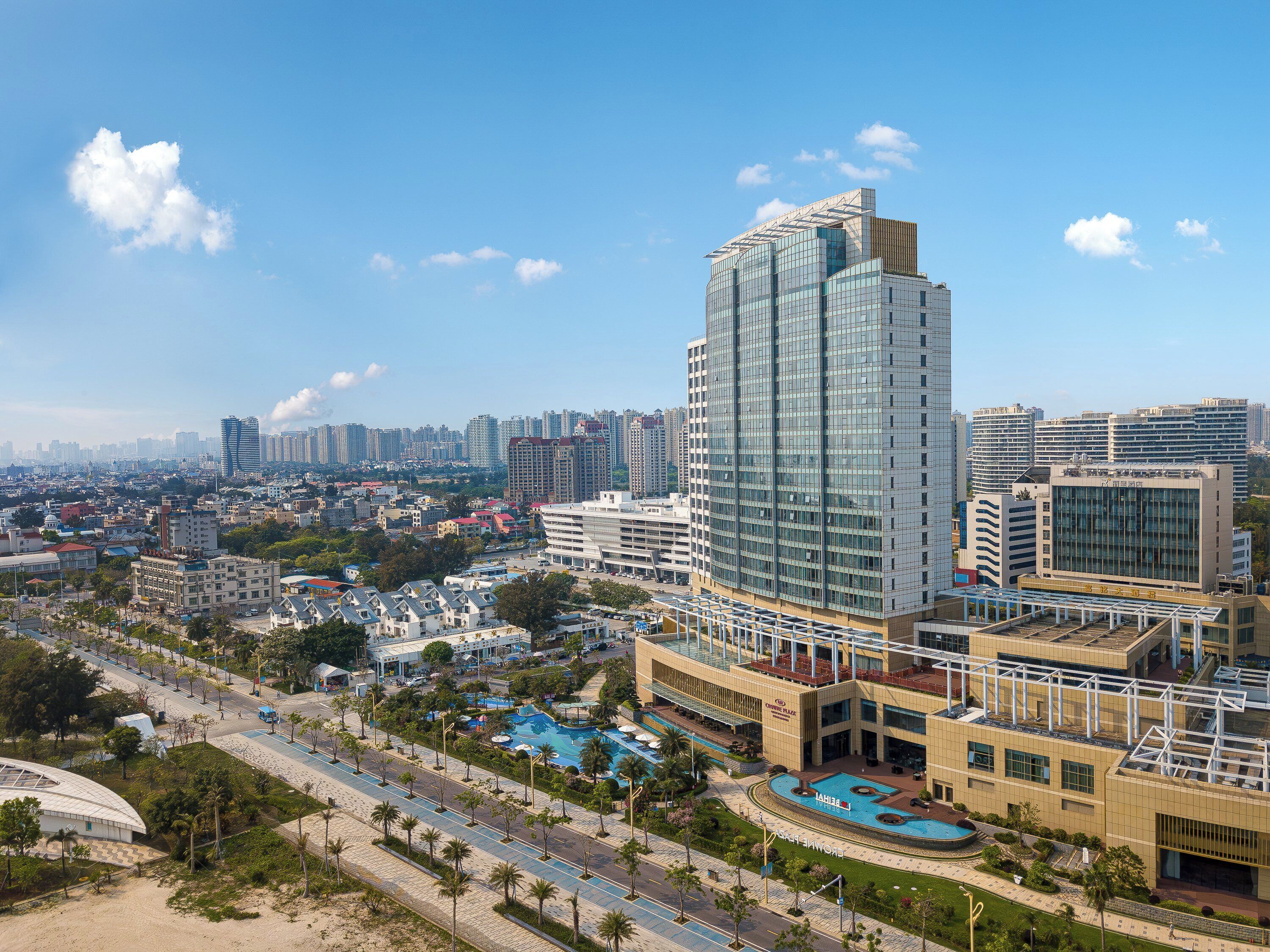 A modern hotel with a large glass facade, a swimming pool, and a landscaped courtyard.