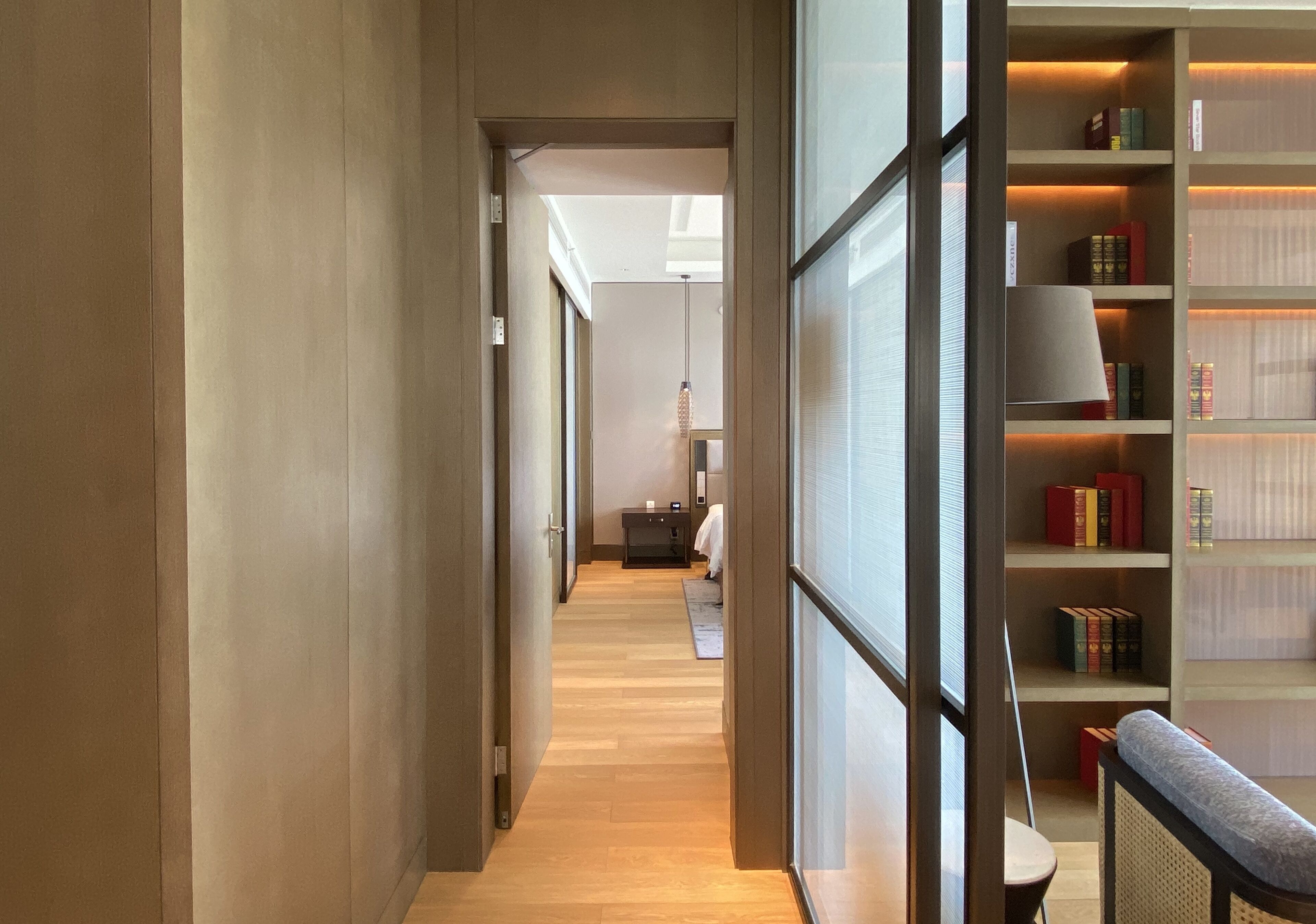 A hallway with a wooden floor, a bookshelf with books, and a lamp.