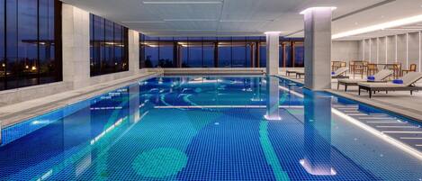 Una amplia piscina interior con agua cristalina, rodeada de grandes ventanales y arquitectura moderna.