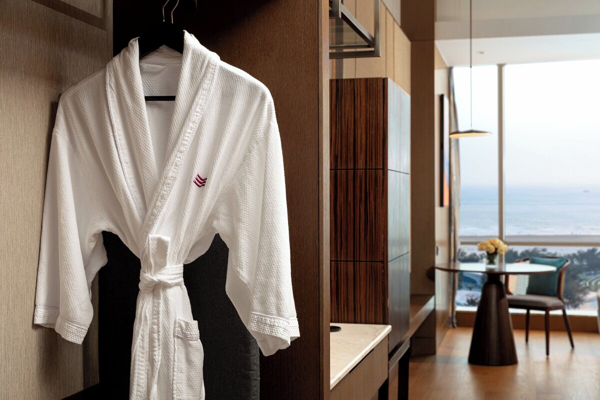 A white robe hanging on a wooden hanger in a modern room with a large window overlooking a scenic view.
