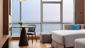 Una habitación de hotel con un ventanal grande, una mesa de comedor con sillas, un sofá y una cama.