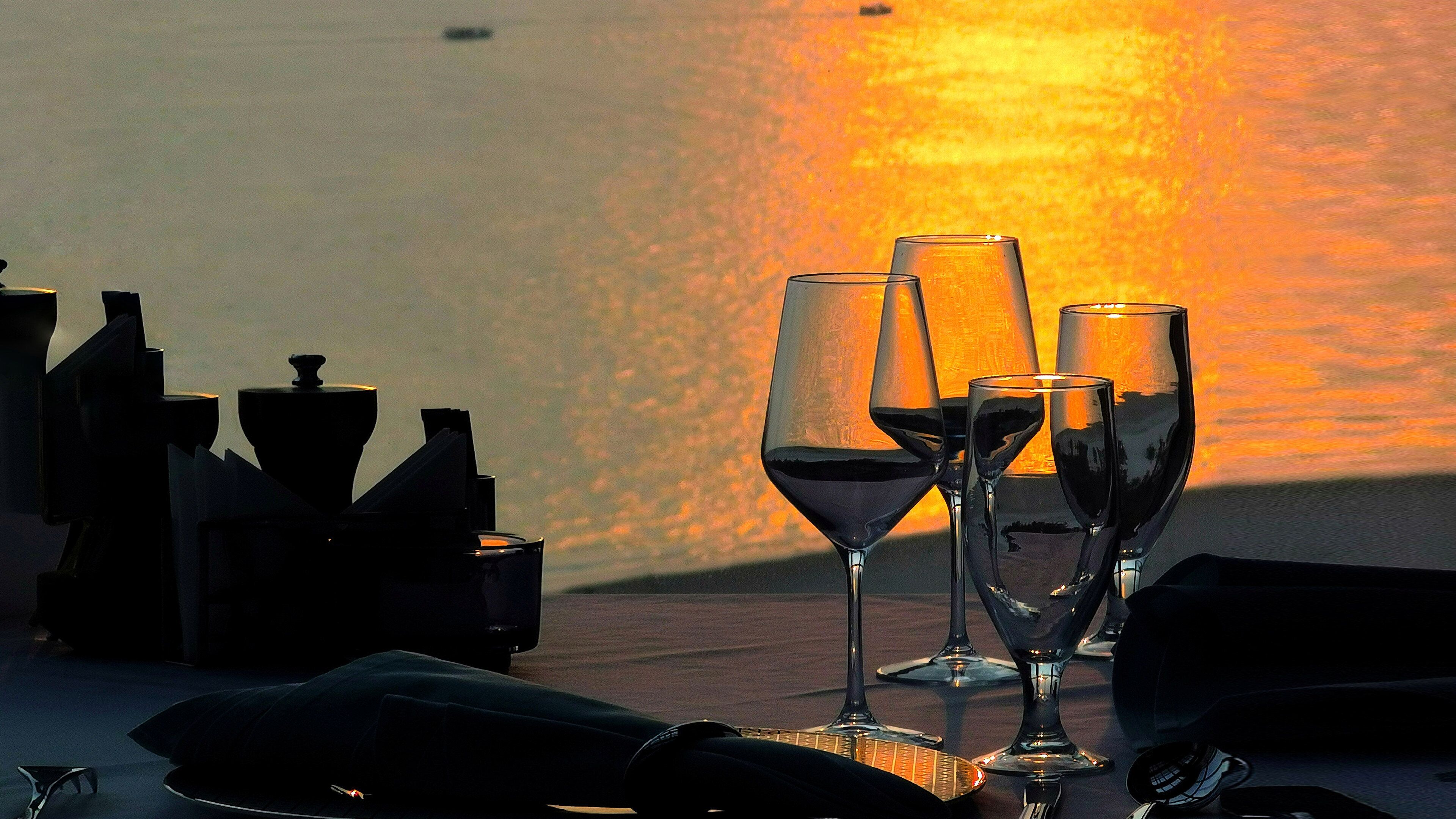 A table set for a meal with wine glasses and bottles, overlooking a sunset.