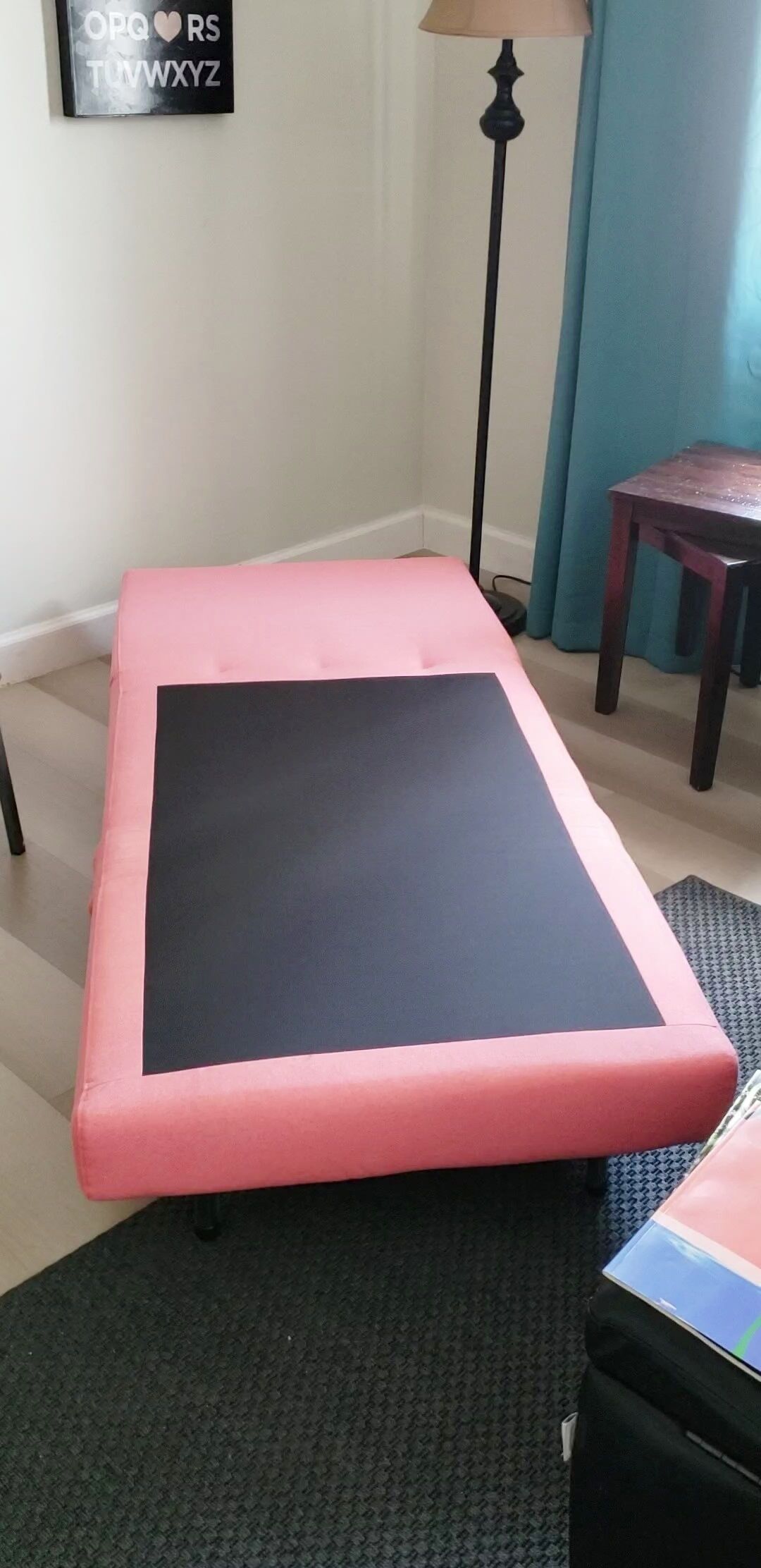 Une pièce avec un banc rembourré rose, une lampe, une petite table et un tapis à motifs.
