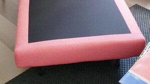 Ein Zimmer mit einer rosafarben gepolsterten Bank, einer Lampe, einem kleinen Tisch und einem Teppich mit Muster.