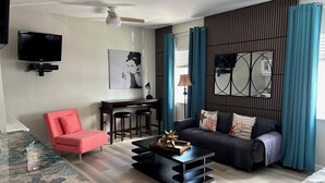 Ein modernes Wohnzimmer mit einer Couch, einem roten Sessel, einem Couchtisch, einem Fernseher und einem Schreibtisch mit einer Lampe.