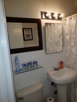 Un bagno con un lavandino bianco, un quadro incorniciato sopra lo specchio e uno scaffale con articoli da toilette.