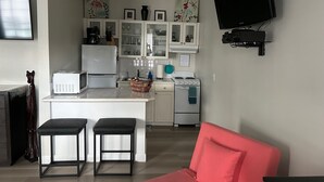 Eine kompakte Küche mit einer zentralen Kochinsel, ein Essbereich mit zwei Hockern, ein rotes Sofa und ein an der Wand befestigter Flachbildfernseher.