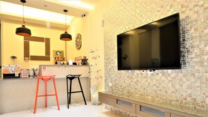 A modern kitchen with a large TV, two bar stools, and a decorative wall. - Sun Day B&B (Magong)