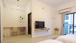 A modern hotel room with a bed, a TV, a desk with chairs, a small plant, and a window with curtains. - Sun Day B&B (Magong)