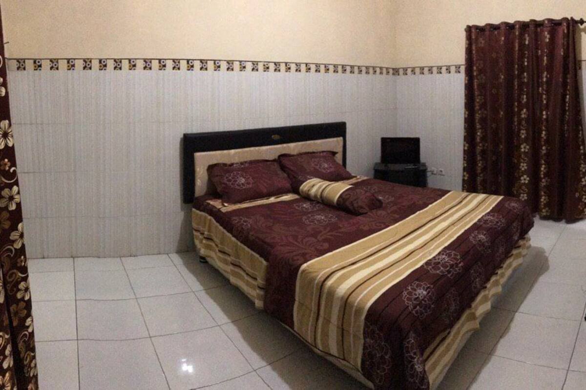 A bedroom with a bed, curtains, a bedside table, and a mirror.