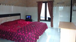 A bedroom with a bed, a TV, a window with curtains, and a wooden nightstand. - Balqis Home Stay (Ngadisari)