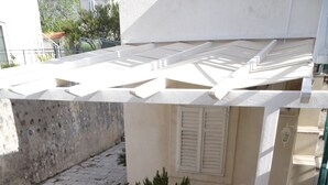 Une terrasse avec une table et des chaises, entourée de plantes en pot et d’une rambarde.
