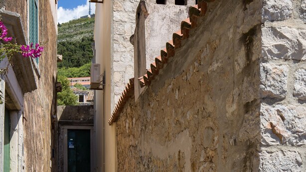 Un escalier étroit en pierre mène à un bâtiment doté d’un toit en tuiles et d’une fenêtre avec des volets.