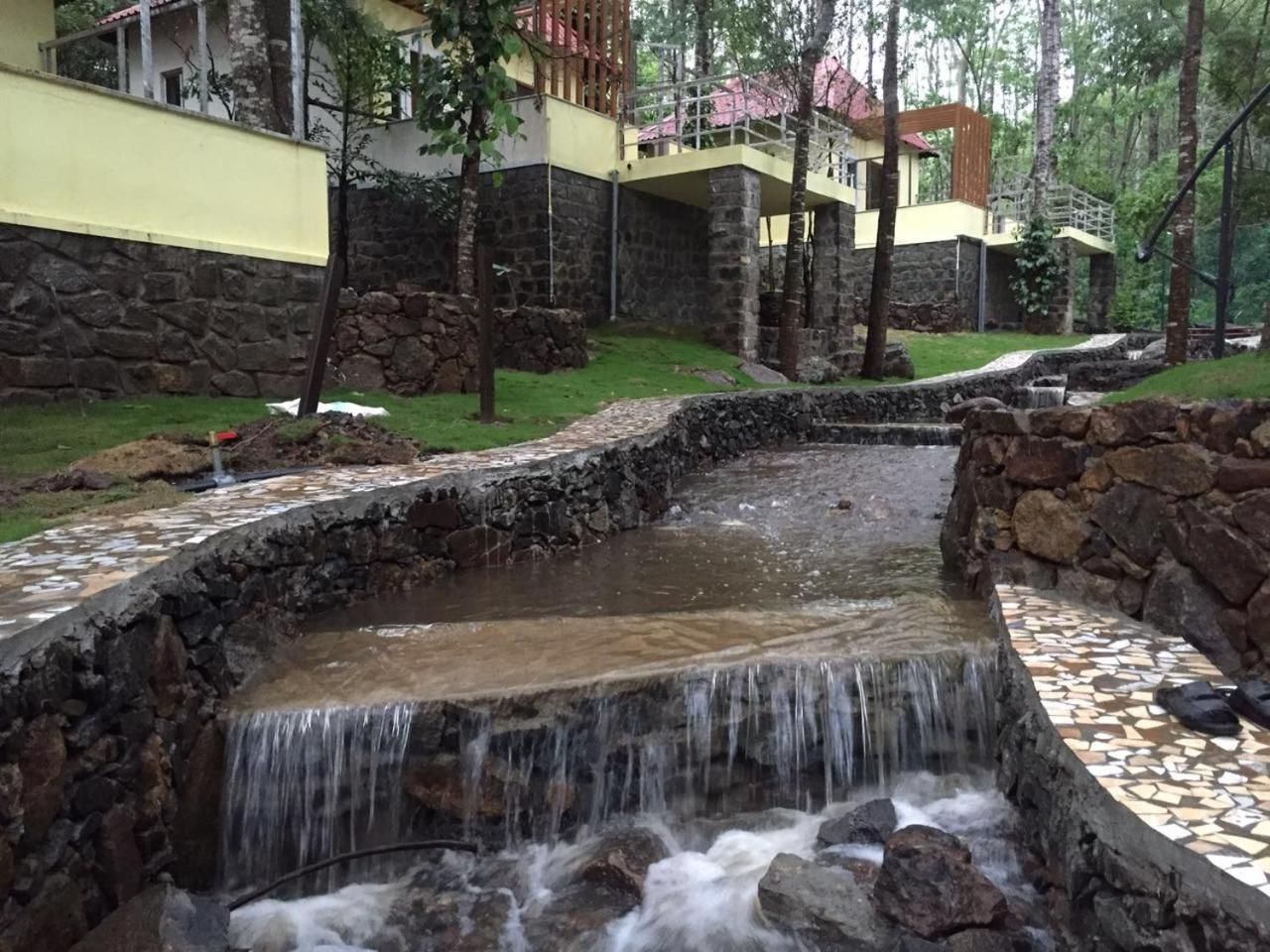 A stone water feature with a small waterfall, surrounded by a stone wall and a tiled walkway.