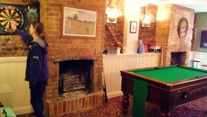 A billiards table, a dartboard, and a fireplace in a room with brick walls. - Dover Adventure Backpackers (Dover)