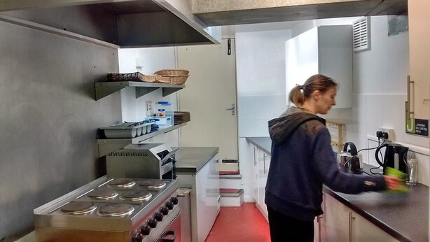 A modern kitchen with stainless steel appliances, a red floor, and a person preparing food. - Dover Adventure Backpackers (Dover)