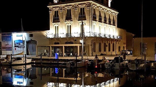 A large, illuminated building with a symmetrical facade, multiple balconies, and a reflection in the water. - Studio LE COLONEL, in the heart💖of the beautiful village of Marseillan  (Marseillan)