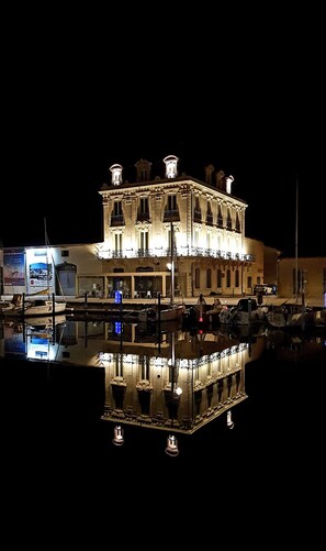 Ein großes, beleuchtetes Gebäude mit einer symmetrischen Fassade, mehreren Balkonen und Spiegelung im Wasser.