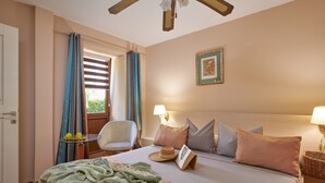 Une chambre d’hôtel avec un lit, une chaise, une table avec des fruits, une lampe et une fenêtre avec des rideaux.