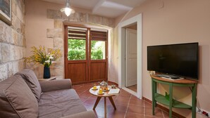 Un salon confortable avec un canapé, une table basse sur laquelle se trouve un plateau avec divers objets, un téléviseur posé sur un meuble et un mur en pierre.