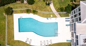 Vue aérienne d’une piscine à bordures courbes, entourée d’une terrasse blanche agrémentée de chaises longues et d’une petite table placée au bord de la piscine.