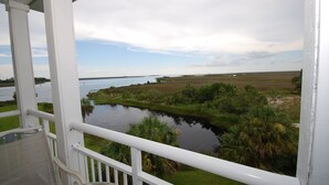 A view from a balcony overlooking a river, with a grassy area and trees in the foreground. - Gulf Breeze Condo #207- Private Boat Ramp! WiFi! Docks to be completed May 2026! (Steinhatchee)