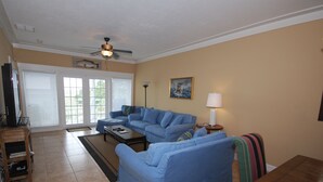 A living room with a blue sofa, a coffee table, a lamp, and a painting on the wall. - Gulf Breeze Condo #207- Private Boat Ramp! WiFi! Docks to be completed May 2026! (Steinhatchee)