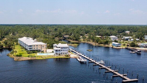 A waterfront property with multiple buildings, a dock extending into the water, and a clear view of the surrounding forest. - Gulf Breeze Condo #207- Private Boat Ramp! WiFi! Docks to be completed May 2026! (Steinhatchee)