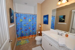 Une salle de bain avec un rideau de douche orné d’un motif sous-marin, des toilettes blanches, un lavabo avec un miroir et un porte-serviettes.
