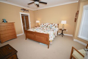 Une chambre à coucher comprenant un lit, deux tables de chevet, une commode, un ventilateur de plafond et une porte.