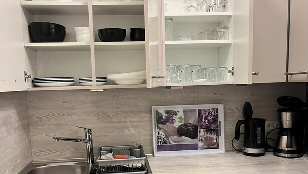 Una cocina moderna con armarios blancos, un lavamanos de acero inoxidable y una cafetera integrada.