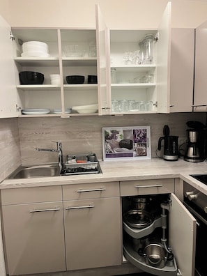 Una cocina moderna con armarios blancos, un lavamanos de acero inoxidable y una cafetera integrada.