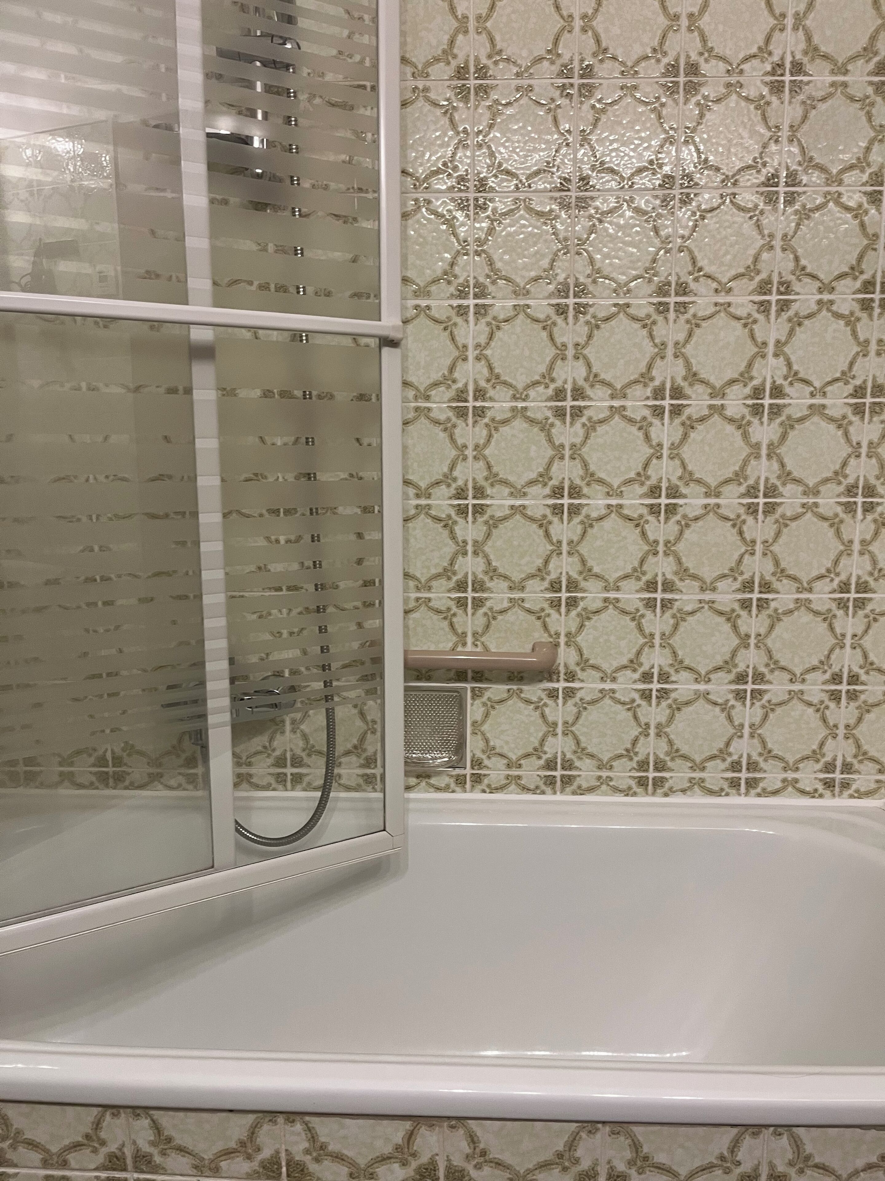 A bathroom with a bathtub, a glass shower enclosure, and patterned tiles on the walls.