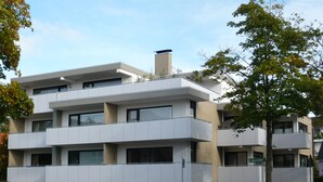 Un edificio moderno de varios pisos con techo plano, ventanas amplias y un estacionamiento con dos coches.