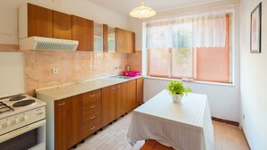 A kitchen with wooden cabinets, a gas stove, a sink, and a window with blinds. - Apartments Sany - Two Bedroom Apartment with Balcony and Sea View (Cavtat)