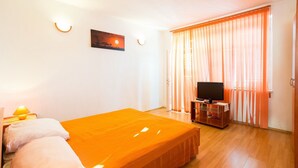 A hotel room with a bed, a television on a stand, a painting on the wall, and a window with curtains. - Apartments Sany - Two Bedroom Apartment with Balcony and Sea View (Cavtat)