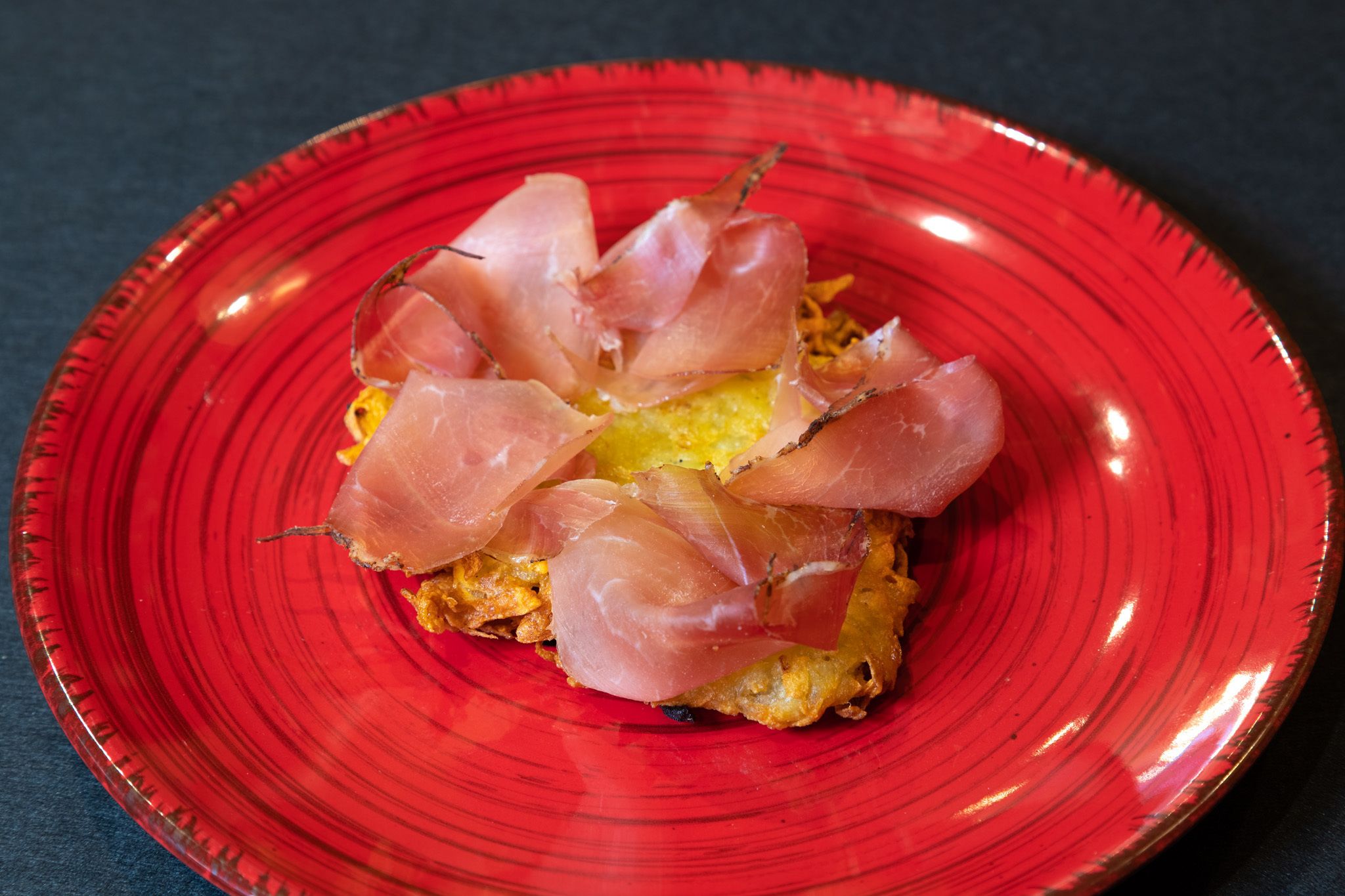 A red plate with a dish containing a yellow base and thinly sliced pink meat.