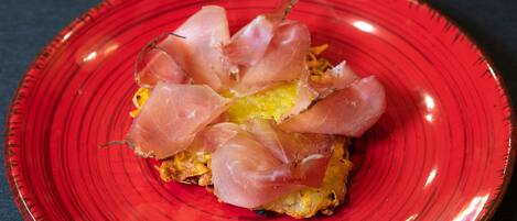 A red plate with a dish containing a yellow base and thinly sliced pink meat.