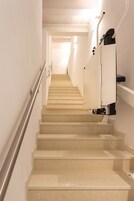 A staircase with a handrail, leading to a landing with a light fixture and a control panel.