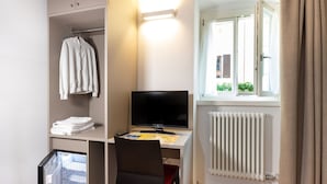 Una habitación pequeña con escritorio, silla, televisor, radiador y ventana con cortinas.