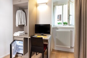 A compact room with a desk, a chair, a television, a radiator, and a window with curtains.