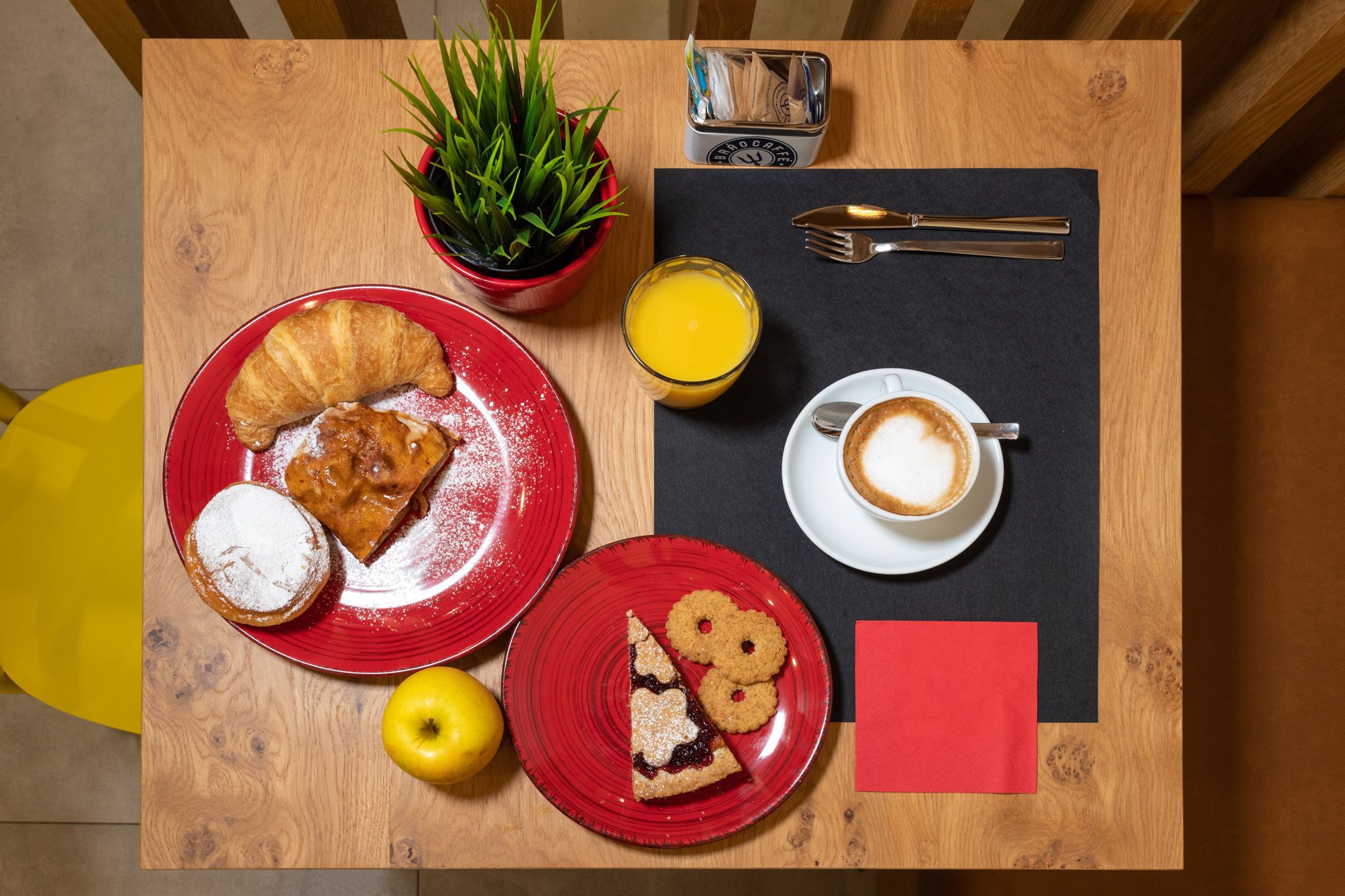 Una mesa de desayuno con cruasanes, galletas, un vaso de zumo de naranja y una taza de café.