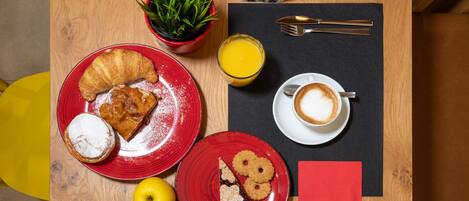 A breakfast table with croissants, cookies, a glass of orange juice, and a cup of coffee.